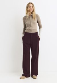 Beige svetr na zip s žebrovaným lemem a dlouhými rukávy, v kombinaci s volnými vínovými kalhotami s kapsami. Model má na sobě béžové espadrilky.