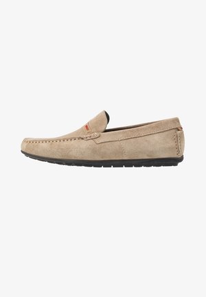Mocassin en suède beige avec un bout cousu et une semelle en caoutchouc noir. Présente un petit accent de logo rouge sur le côté. Design décontracté.