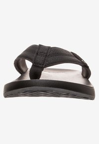 Sandale en tongs noire avec des brides synthétiques texturées, une semelle plate et un motif de sculpture subtil au fond pour une meilleure adhérence.