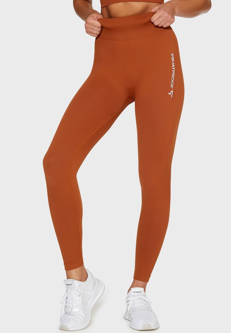 Prążkowane legginsy o wysokim stanie w kolorze spalanej pomarańczy. Charakteryzują się designem odpornym na przysiady oraz białym logo na lewej nogawce. Teksturowana tkanina.