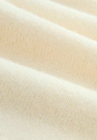 Tessuto fine a maglia color crema con una superficie morbida e testurizzata, caratterizzato da sottili variazioni di tonalità e motivo, ideale per abbigliamento o tappezzeria.