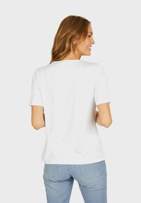 Weißes Baumwoll-T-Shirt mit kurzen Ärmeln und rundem Halsausschnitt, das ein einfaches, klares Design und eine glatte Textur aufweist.
