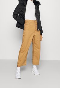 Černá huňatá bunda s umělou kožešinou, bílý rolák a béžové kalhoty s širokými nohavicemi. Bílé tenisky doplňují celkový vzhled. Jednoduchý a ležérní design.