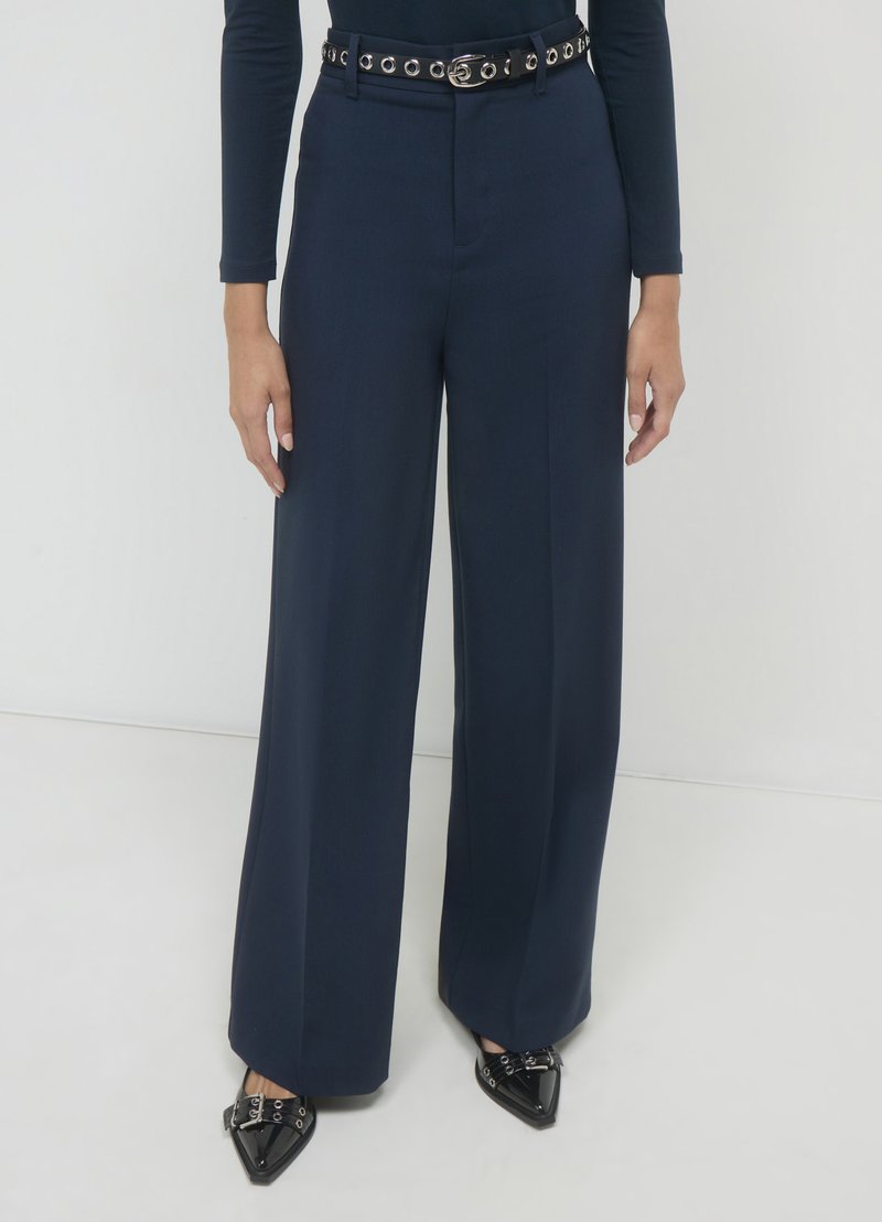 Pantalons en navy àLargeur ample avec taille haute et ceinture à œillets en argent. Le tissu texturé, le devant plat et la coupe ajustée mettent en valeur la silhouette.