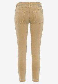 Jean slim beige vu de dos avec deux poches arrière et un petit patch cousu sur la ceinture.