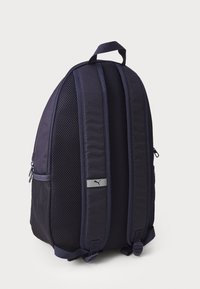 Mochila azul marino con correas de hombro acolchadas y de malla, y un asa en la parte superior. Presenta un bolsillo con cremallera y un acento de logo plateado.
