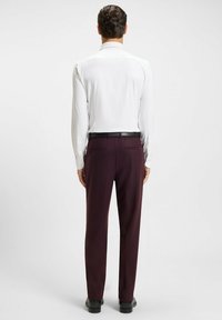 Herenoutfit met een witte lange mouwen shirt en donker bordeauxrode broek. De broek heeft een soepele textuur en twee achterzakken. Inclusief zwarte riem.