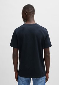 Dark navy short-sleeve t-shirt made of cotton. Features a classic crew neck and a relaxed fit, displayed from the back with light blue jeans.