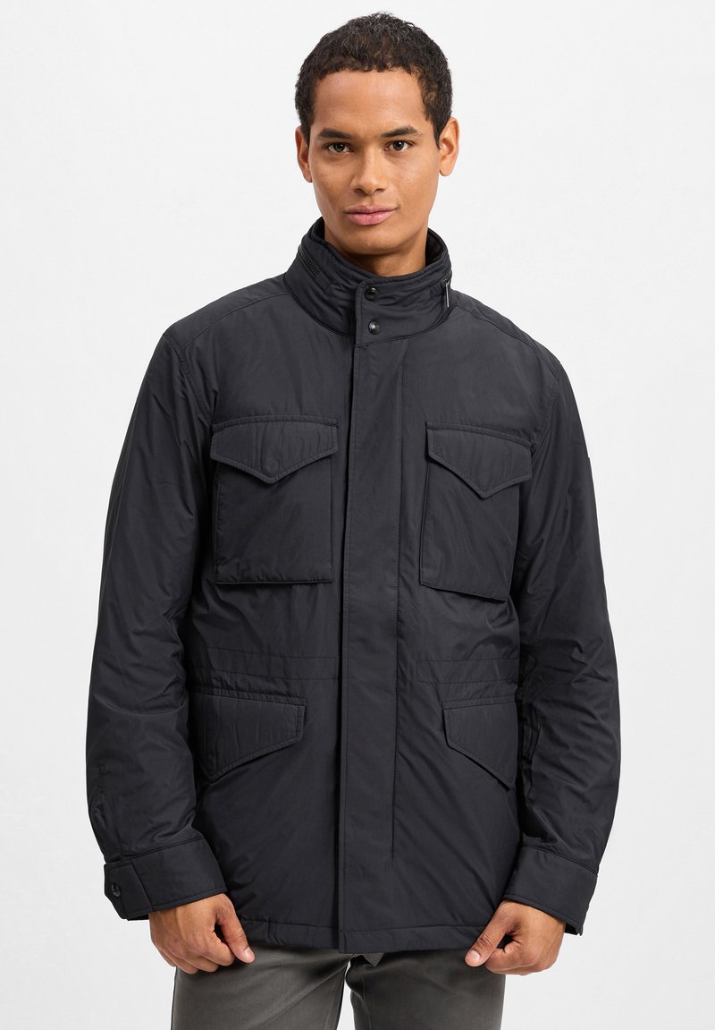 Svart, vadderad jacka med hög krage, tryckknappar och fyra framfickor. Slät textur med matt finish. Justerbara manschetter.