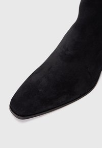 Sorte semskede ankelstøvler med spiss tå, slank silhuett og jevn tekstur. Har en diskret matt overflate og en tynn såle.