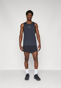 Tumši zils bezroku tops ar nenozīmīgu logotipu, kopā ar melniem sporta šortiem. Valkāts ar melniem sporta apaviem un baltām zeķēm.