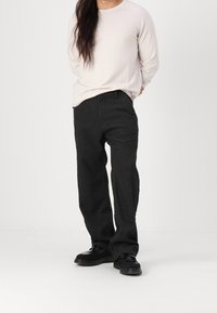 Dunkelgraue, locker sitzende Hose aus strukturiertem Stoff, kombiniert mit einem hellbeigen langärmeligen Shirt und schwarzen Schuhen. Einfaches Design und gerader Schnitt.