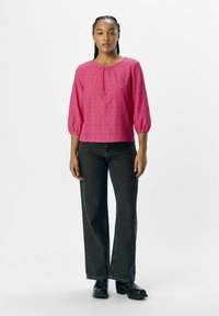 Blouse rose texturée avec des manches bouffantes 3/4 et un col rond, associée à un jean noir à jambes larges et des bottes noires.