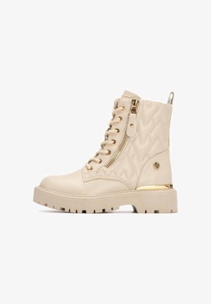 Bottes de combat beiges en cuir avec un design matelassé, dotées de quincaillerie dorée, d'une fermeture éclair latérale et d'une semelle épaisse et texturée.