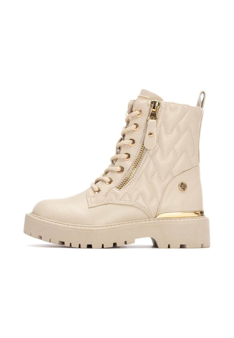 Bottes de combat beiges en cuir avec un design matelassé, dotées de quincaillerie dorée, d'une fermeture éclair latérale et d'une semelle épaisse et texturée.