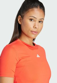 Camiseta atlética roja de mangas cortas, hecha de un material suave. Presenta un logo triangular blanco en el pecho.