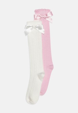 Calze fino al ginocchio bianche e rosa. La calza bianca presenta un design a treccia testurizzato con un bordo ondulato e un fiocco in raso. La calza rosa è liscia.