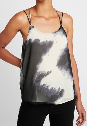 Vrouw draagt een zwart-wit tie-dye mouwloze top met dunne dubbele schouderbandjes, gecombineerd met zwarte broek.