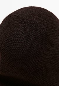 Close-up of dark brown knitted fabric with a textured, looped pattern and a small central seam or twist at the top.