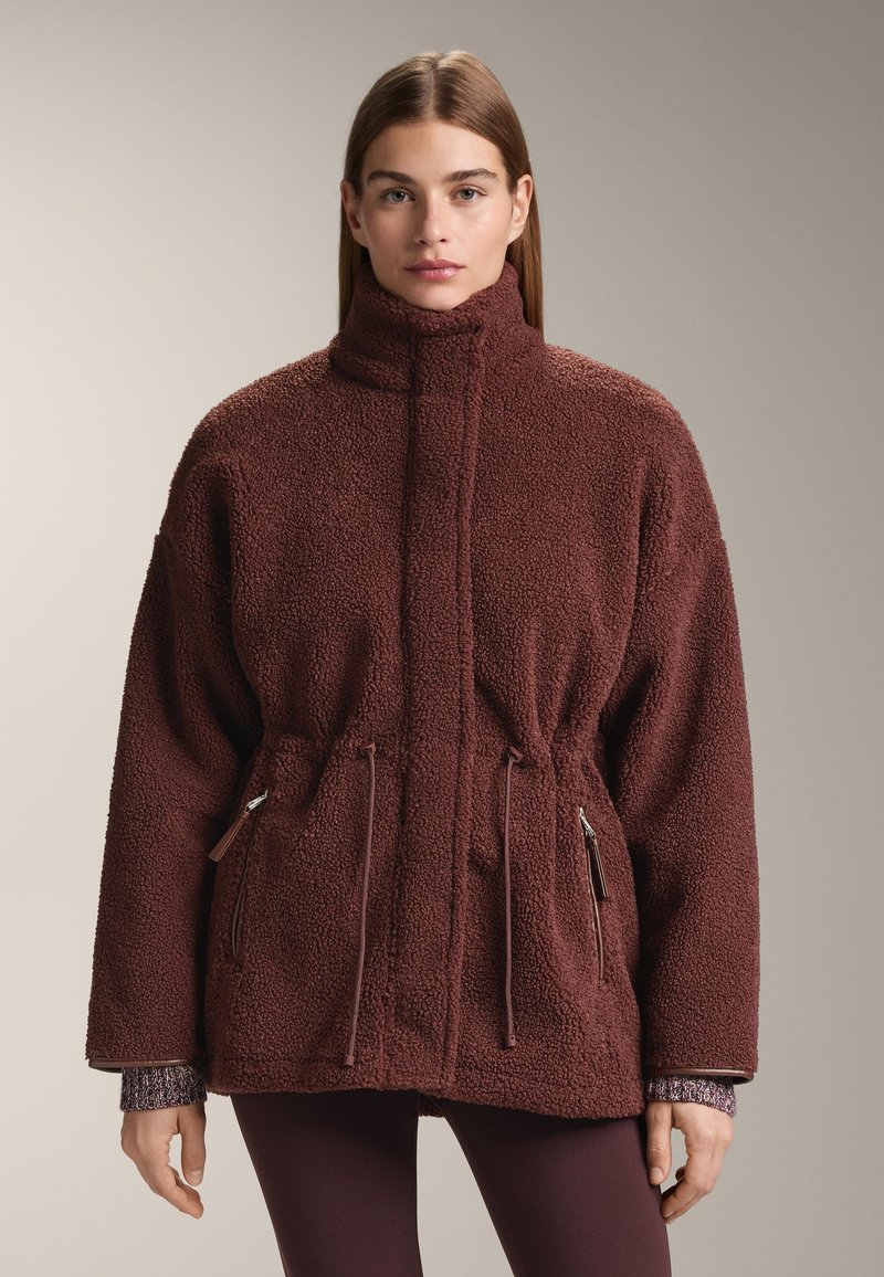 Burgundská fleecová bunda s vysokým límcem, stahováním v pase a kapsami na zip. Má texturovaný povrch a volnější střih.