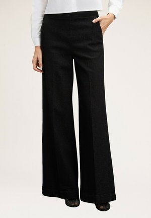 Pantaloni neri a gamba larga realizzati in un tessuto strutturato e con vita alta, dotati di un orlo curato e tasche laterali. Abbinati a una blusa bianca.