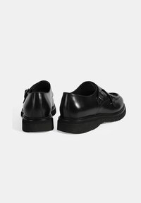Black leather shoes with a smooth texture, featuring a round toe, dual buckles, and a thick black rubber sole.
