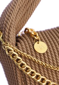 Bolso de texturizado tejido en tono beige con una cadena de oro y un charm. El diseño incluye un material suave y flexible con un patrón de trenzado distintivo.