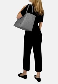 Grau gewebe Tasche mit quadratischem Design und strukturierten Oberfläche, ausgestattet mit zwei stabilen Griffen. Sichtbares Logo auf einer Seite.