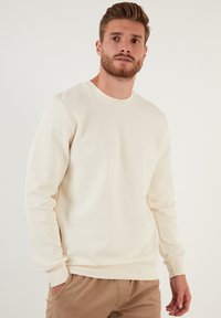 Lichtbeige crew neck sweatshirt van textuurstof, met lange mouwen en geribbelde manchetten. Casual gedragen met lichtbruine broek.