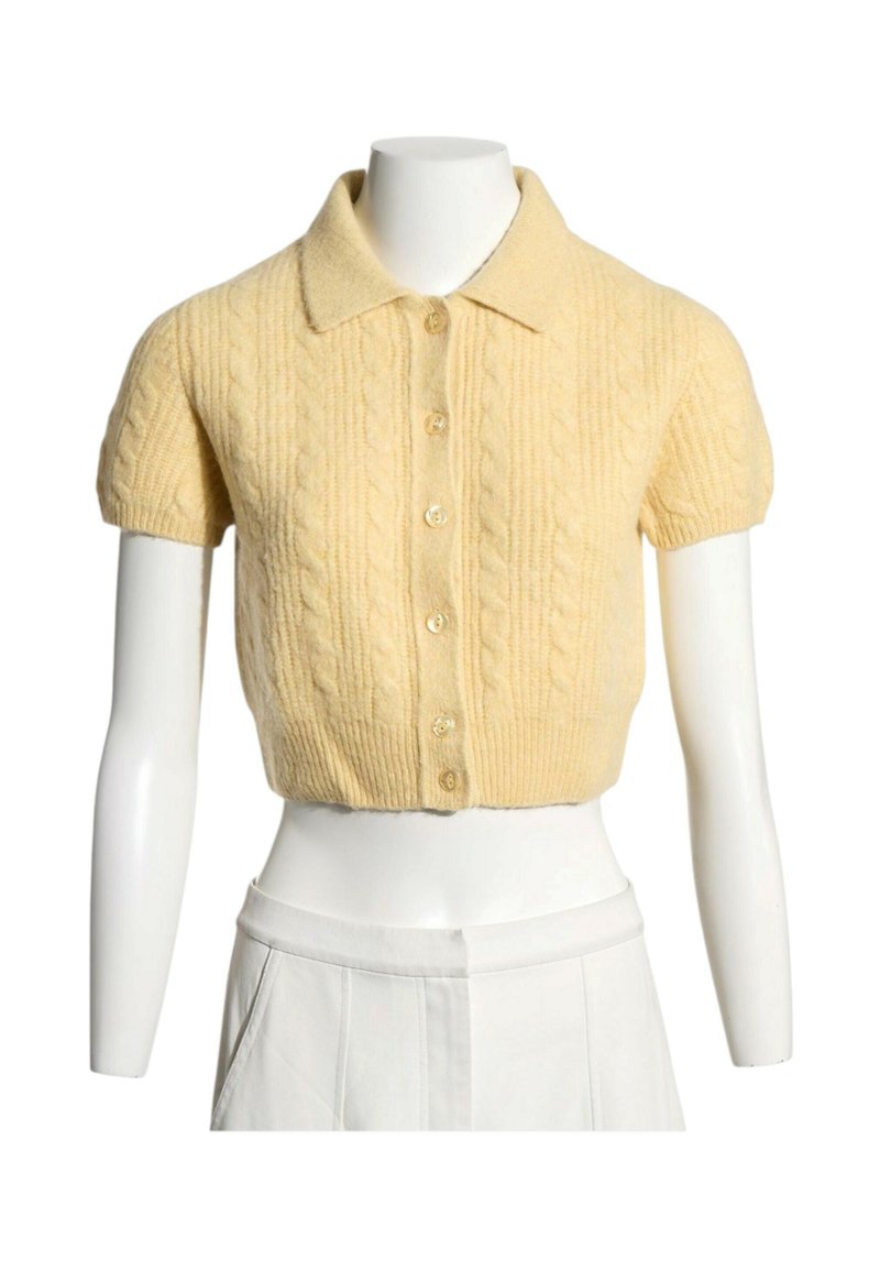 Cardigan court à manches courtes, jaune pâle, en maille torsadée, avec col et boutons à l'avant sur un buste de mannequin blanc.