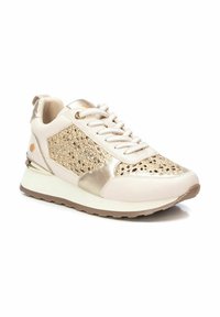 Zapatilla beige con un panel de malla metálica dorada, acentos de cuero suave, cordones texturizados y una entresuela blanca con una suela marrón.