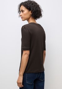 Korte mouwen bruine blouse met een ronde halslijn en subtiele pofmouwen, gemaakt van zachte stof, gecombineerd met blauwe denim jeans.