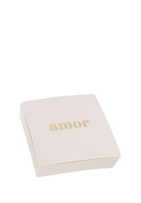 Piccola scatola quadrata di un tenue rosa pallido con il testo dorato "amor" centrato sul coperchio, posata su uno sfondo bianco.