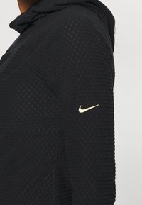 Felpa con cappuccio nera caratterizzata da un motivo testurizzato. Presenta un logo Nike dorato sul maniche sinistro. Progettata per comfort e prestazioni.