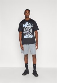 Μαύρη μπλούζα t-shirt με λευκό και μπλε γραφικό κείμενο που γράφει "NIKE HOOPS", συνδυασμένη με γκρι σορτσάκι, μαύρες κάλτσες και μαύρα αθλητικά παπούτσια.