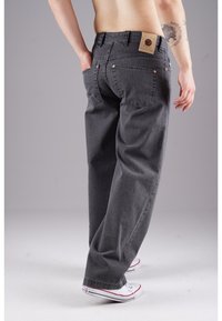 Gray denim pants feature a relaxed fit with a high waist, back pockets, and a branded tag on the waistband. Paired with white sneakers.