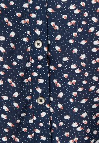 Navy shirt featuring a repeated pattern of white and orange flowers with a polka dot background; includes silver buttons along the front.