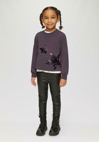 Donkerpaarse sweatshirt met een sterrenontwerp van pailletten, gelaagd over een crèmekleurig topje, in combinatie met zwarte nepleer leggings en zwarte veterschoenen.