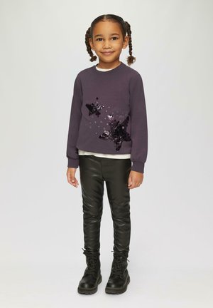 Donkerpaarse sweatshirt met een sterrenontwerp van pailletten, gelaagd over een crèmekleurig topje, in combinatie met zwarte nepleer leggings en zwarte veterschoenen.