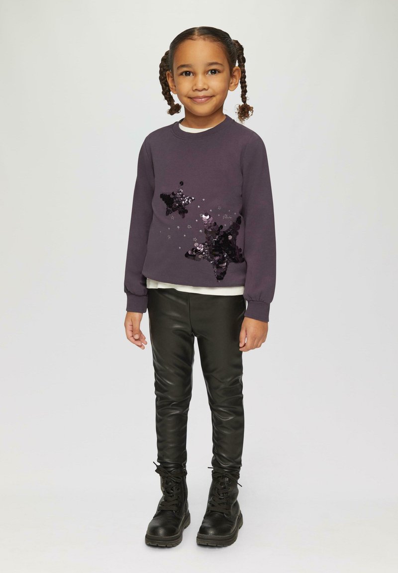 Donkerpaarse sweatshirt met een sterrenontwerp van pailletten, gelaagd over een crèmekleurig topje, in combinatie met zwarte nepleer leggings en zwarte veterschoenen.