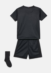 Juoda sportinė apranga su trumpomis rankovėmis, šortais ir juodomis kojinėmis. Yra vertikalios siūlių juostelės ir kontrastingi akcentai ant apykaklės.