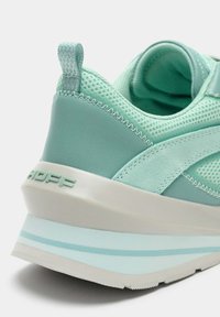 Zapatilla verde menta con malla transpirable y acentos de cuero suave. Talón redondeado con entresuela blanca y logo de la marca en relieve.