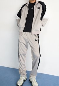 Grå träningsoverall med kontrasterande svarta och vita paneler, zip-up jacka, byxor med elastisk midja, logotypdetaljer, bärs med sportskor.