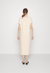 Abito midi beige chiaro con maniche corte, tessuto morbido, spacchi laterali e silhouette dritta, indossato con mule nere con tacco a blocco.