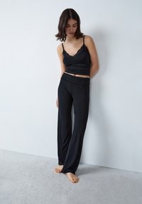 Zwart pyjama set met een aansluitend tanktop met kantafwerking en brede, losvallende broeken. Zachte, gladde stofstructuur.