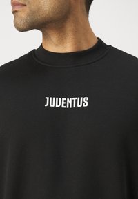 Sudadera negra con cuello redondo. Presenta el texto blanco "JUVENTUS" en el centro. Hecha de un material suave con una textura lisa.