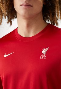 Rotes Nike T-Shirt mit Rundhalsausschnitt, kurzen Ärmeln und einem weißen Liverpool FC-Wappen mit einem Vogel-Logo auf der linken Brust.