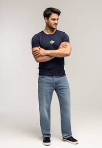 Granatowy t-shirt z krótkim rękawem i białym logo, do tego jasnoniebieskie jeansy o prostych nogawkach i czarne trampki. Prosty i casualowy styl.