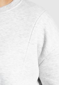 Felpa grigia chiara con una texture morbida, colletto a coste e cuciture delle spalle ripiegate, che enfatizzano una vestibilità rilassata e un design sobrio.
