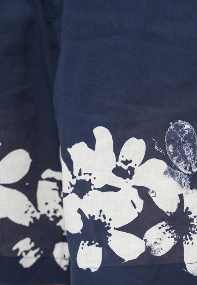 Tissu bleu marine avec de grandes impressions florales blanches et des accents texturés. Le design comprend un mélange de formes de fleurs pleines et en contour.